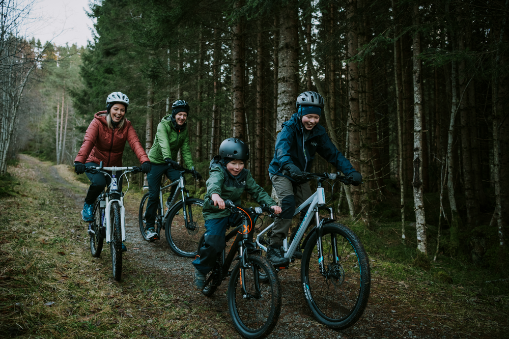 Familie på 4 sykler nedover en skogsvei